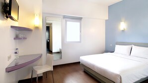 Habitació d'hotel amb llit, escriptori amb cadira, televisió i finestra.