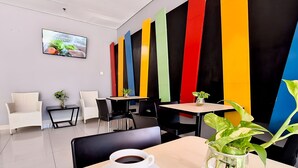 Una cafeteria moderna amb un televisió de pantalla plana que mostra un programa de cuina, panells verticals i de colors a la paret, i una taula amb una tassa de cafè i una planta.