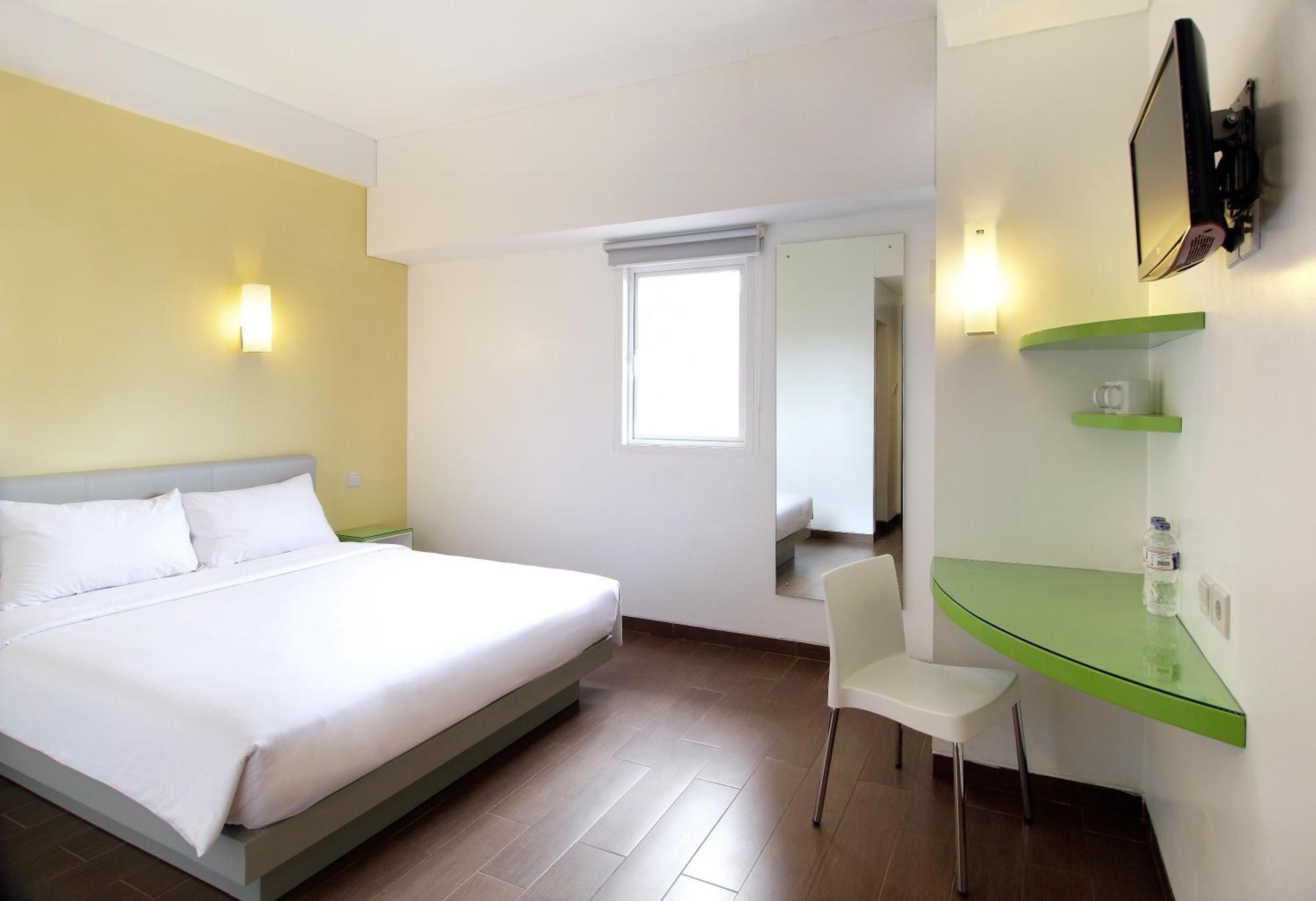 Ein Hotelzimmer mit Bett, Schreibtisch, Stuhl, Spiegel und Fenster.