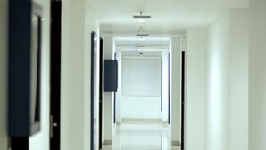 Un passadís llarg i estret amb parets blanques i un sòl brillant, que condueix a una porta amb una finestra.