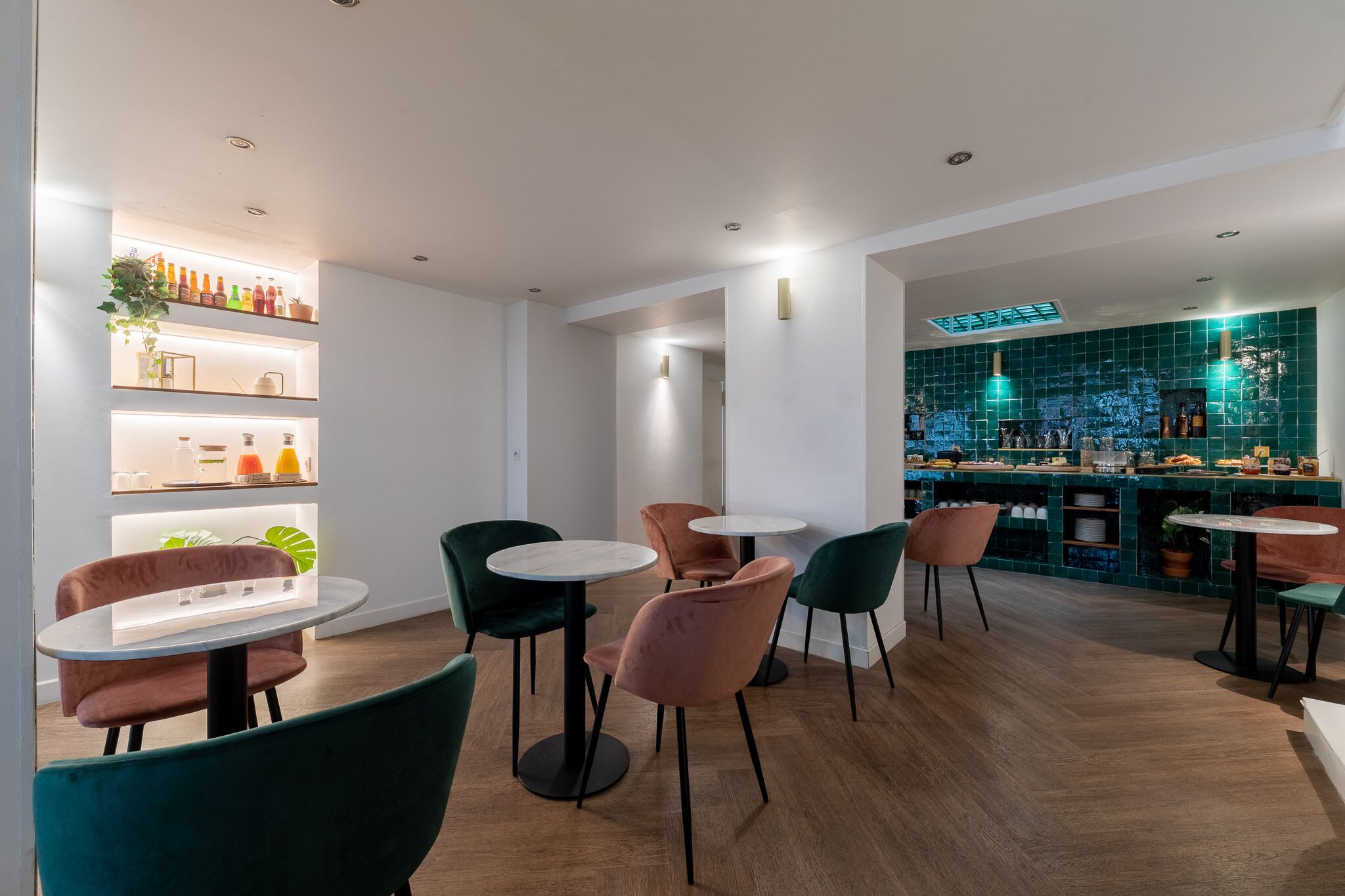 Un espace bar moderne avec des tables et des chaises rondes, des étagères remplies de bouteilles et un mur recouvert de carreaux verts.