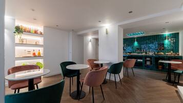 Un área de bar moderna con mesas y sillas redondas, estantes con botellas y una pared revestida de azulejos verdes.
