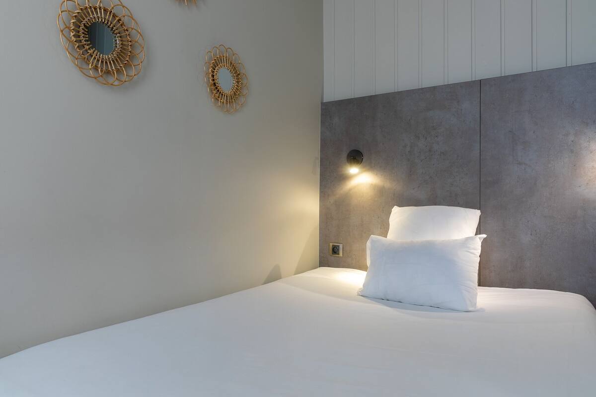 A modern bedroom with a large bed, two wall sconces, and two decorative wall mirrors.