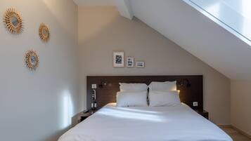 Une chambre moderne avec un plafond en pente, un grand lit avec du linge de lit blanc, une tête de lit en bois, des lampes de chevet et des œuvres d’art accrochées au mur.