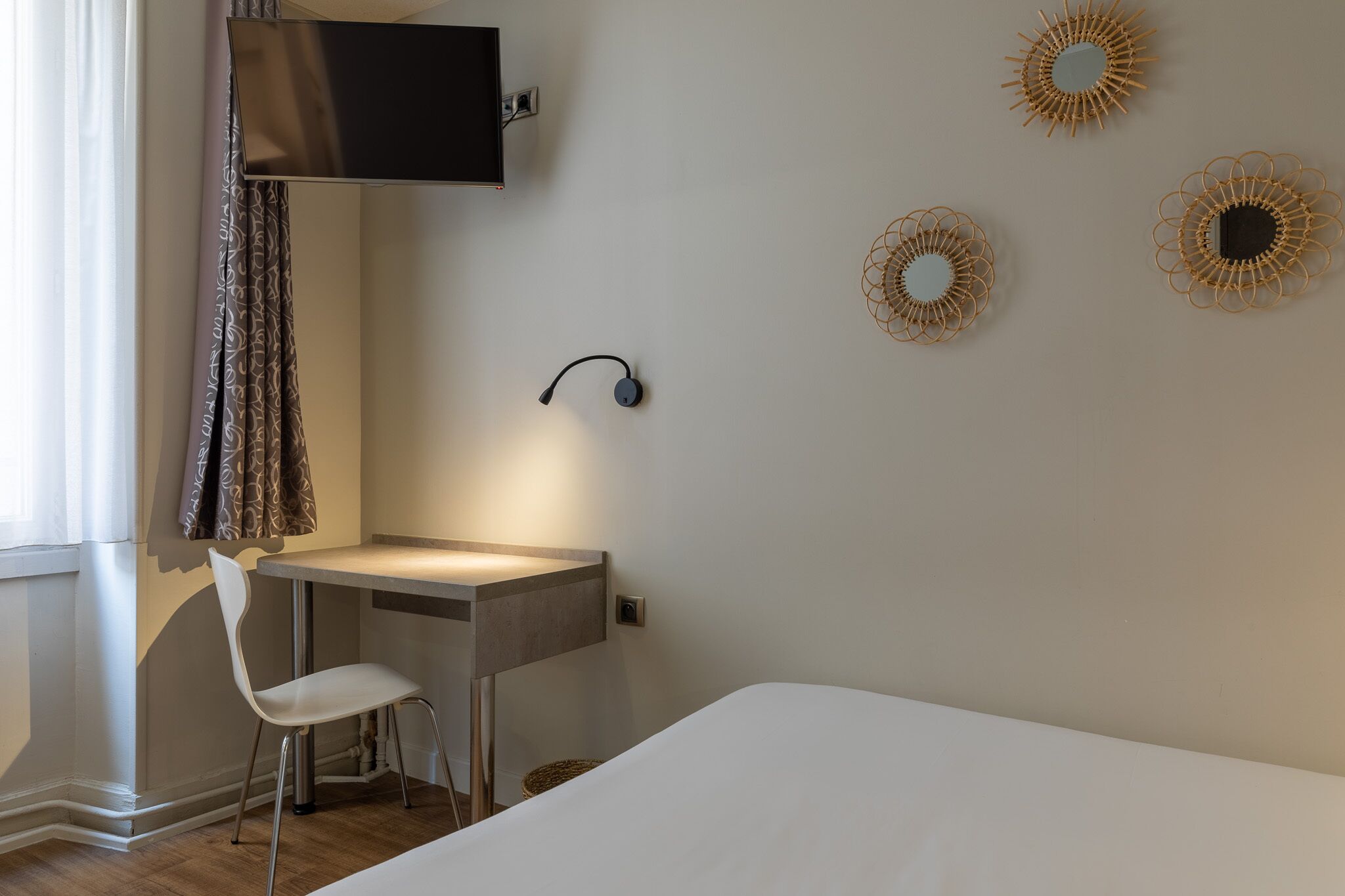 Une chambre à coucher comprenant un lit, un bureau, une chaise, un téléviseur fixé au mur et des œuvres d’art décoratives.