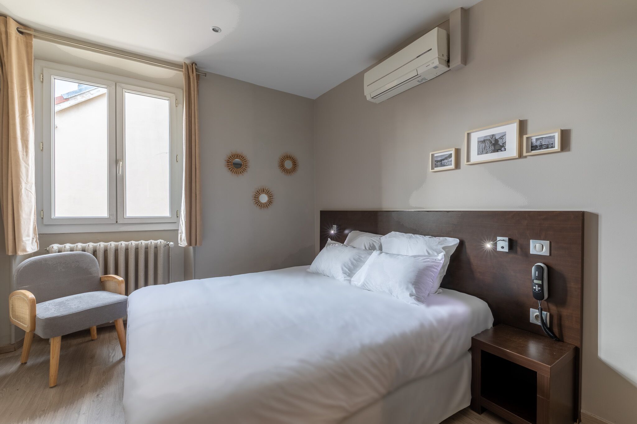 Une chambre à coucher avec un lit, une chaise, une table de chevet avec un téléphone, un radiateur et une fenêtre avec des rideaux.