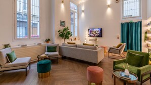 Un salón amplio con un sofá gris, un sillón verde y un reposapiés turquesa.