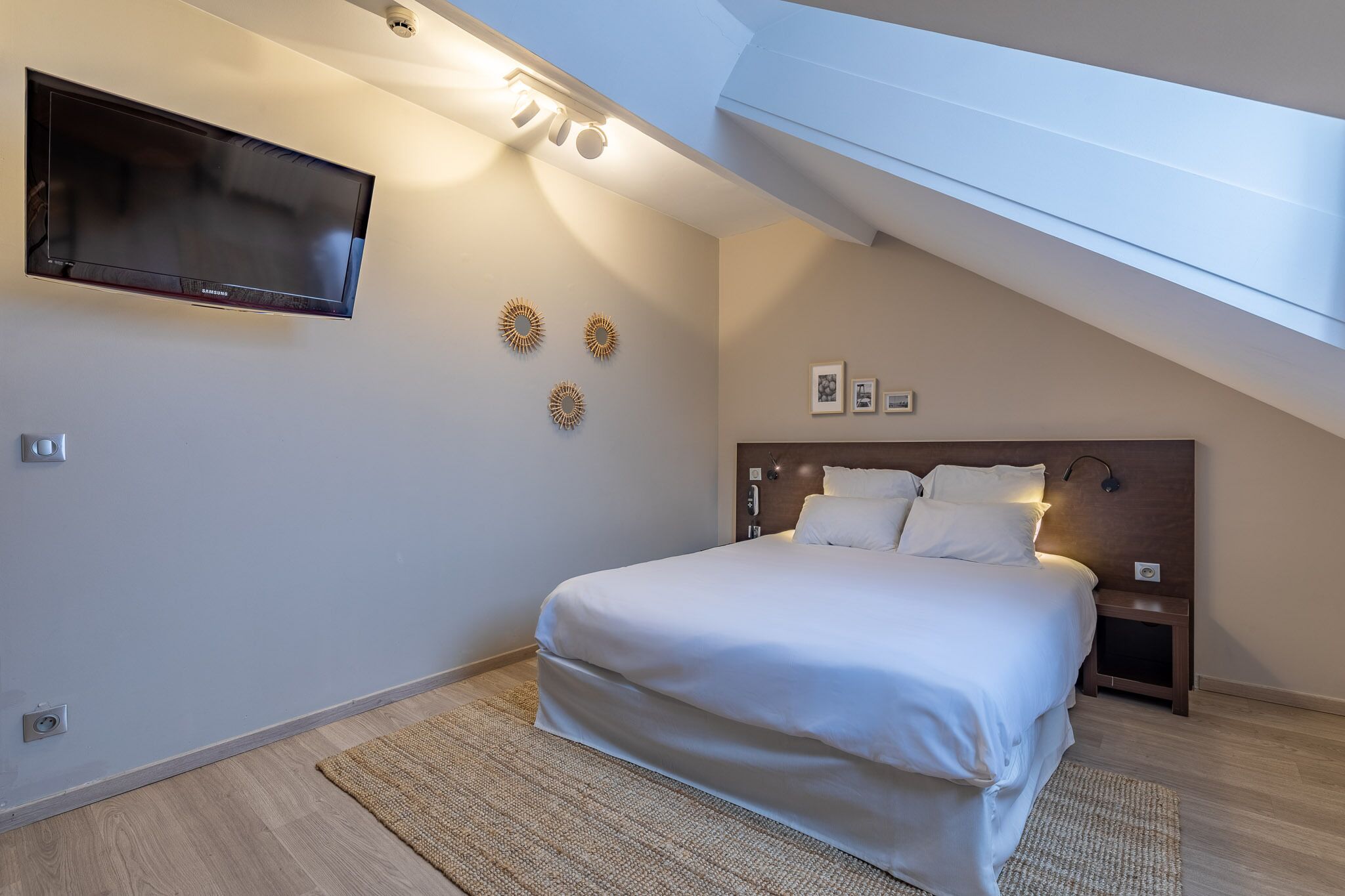 A bedroom with a bed, a TV mounted on the wall, and a skylight.