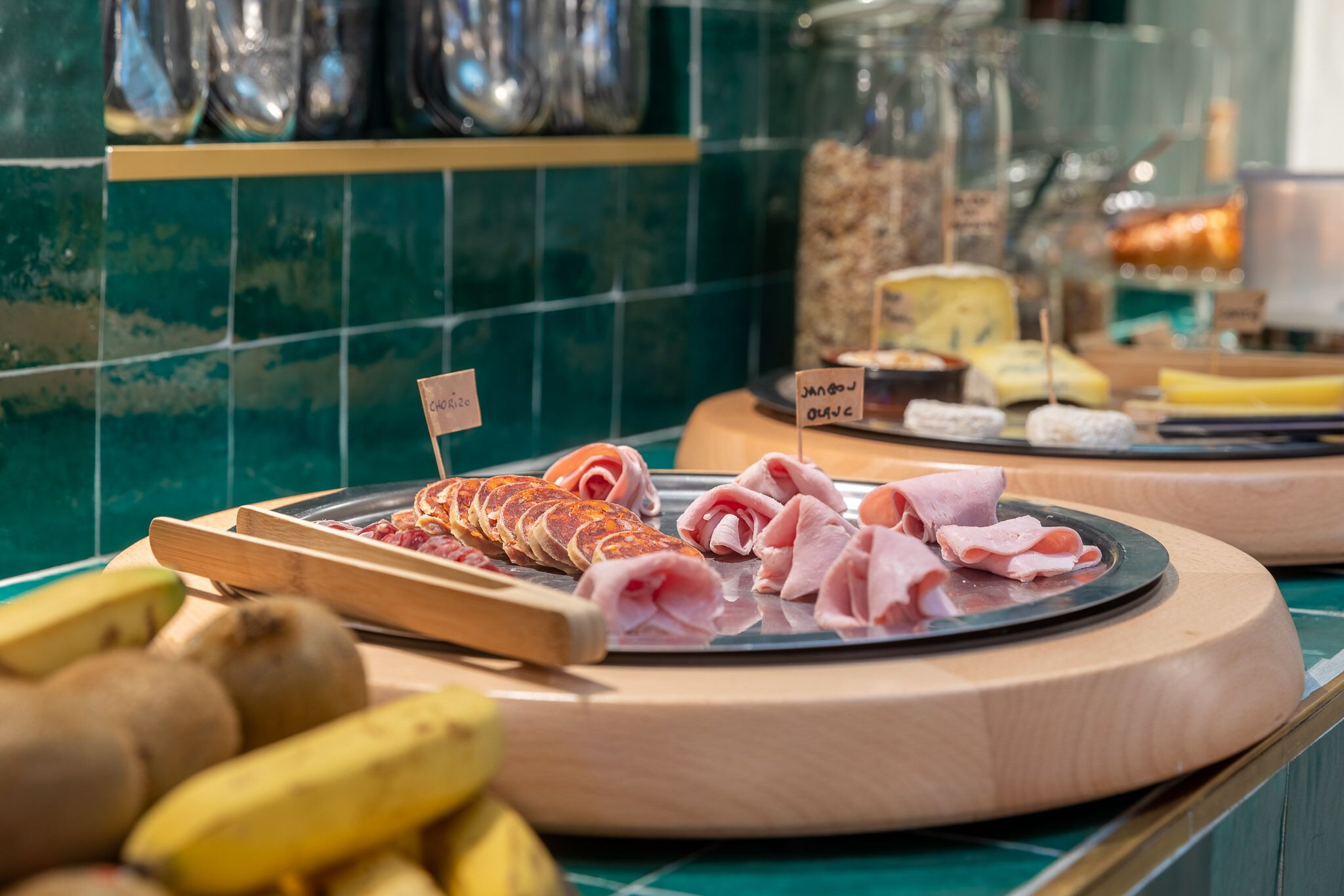 Une planche de charcuterie avec divers types de viandes et de fromages, accompagnée de bananes et de kiwis.