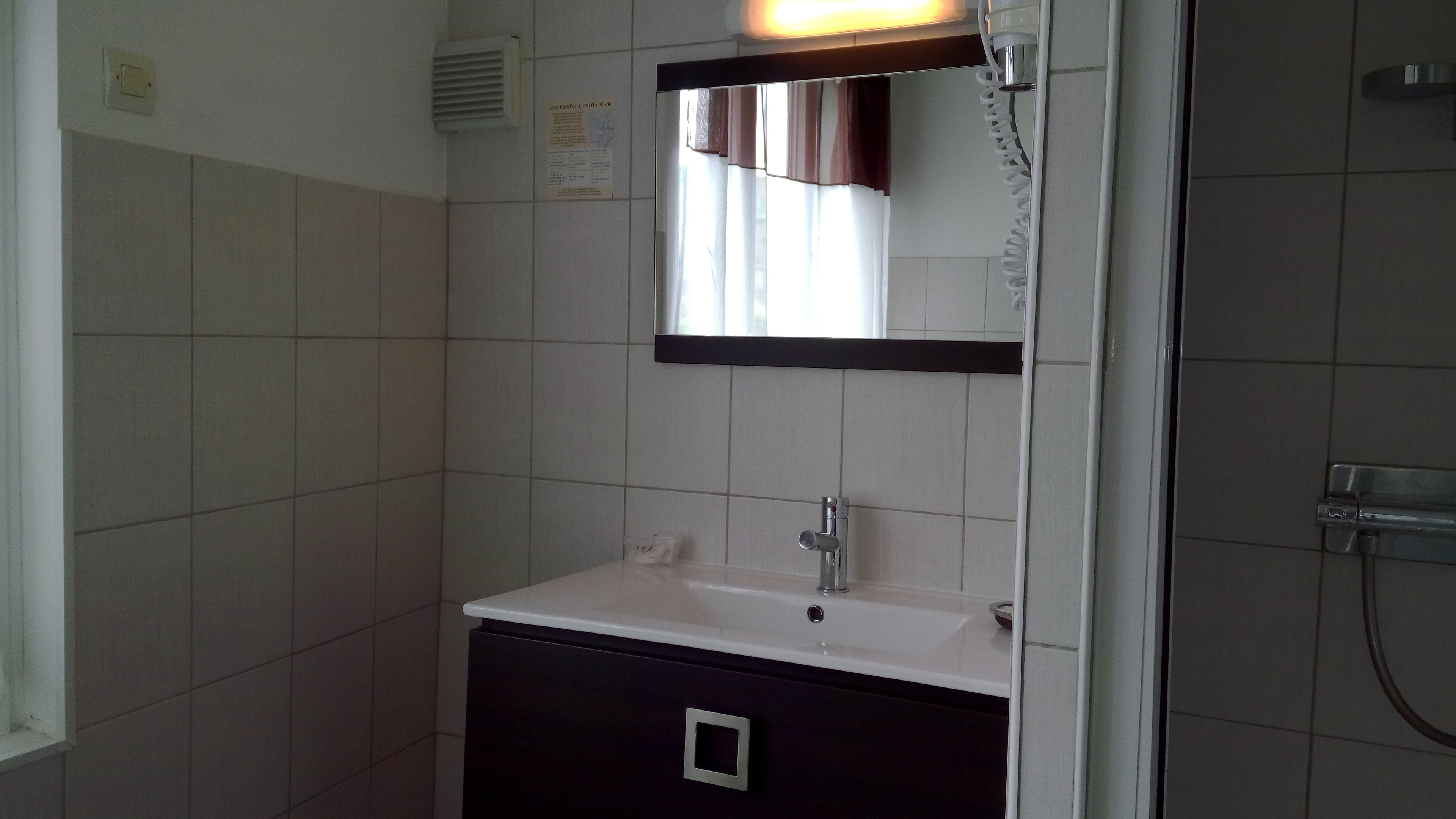 Un baño con lavamanos blanco, espejo y zona de ducha.