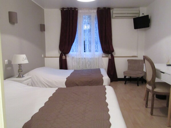 A hotel room with two beds, a desk, a chair, a TV, and a window with curtains.