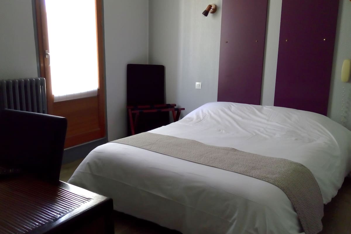 Una habitación de hotel con una cama, un escritorio, una silla, un radiador y una ventana.