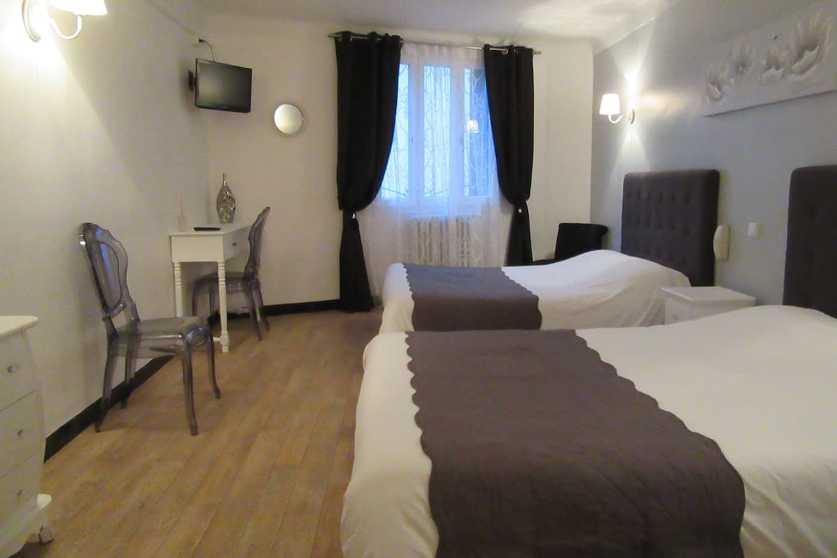 Habitación de hotel con dos camas, un escritorio, una silla y un televisor en la pared.