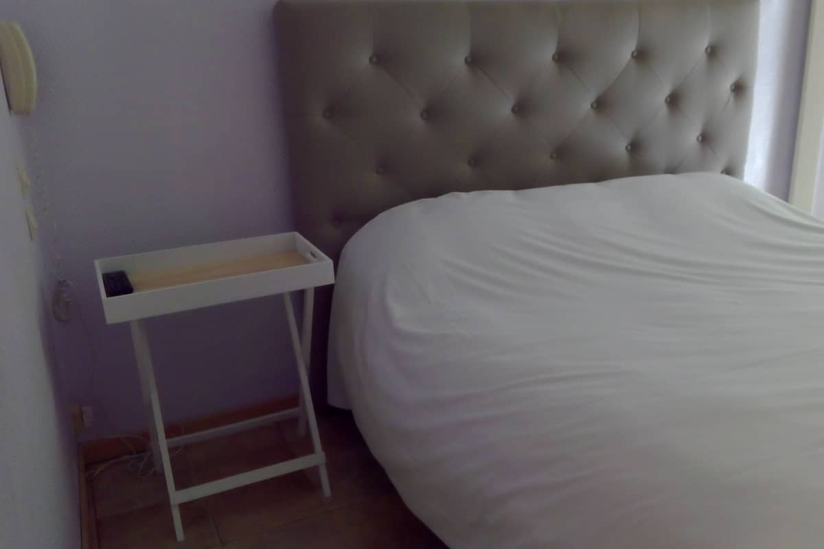 Un dormitorio con cabecera capitonada, mesita de noche blanca y cama bien hecha.