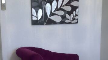 Una habitación con un sofá morado, una silla de madera y una cama blanca.