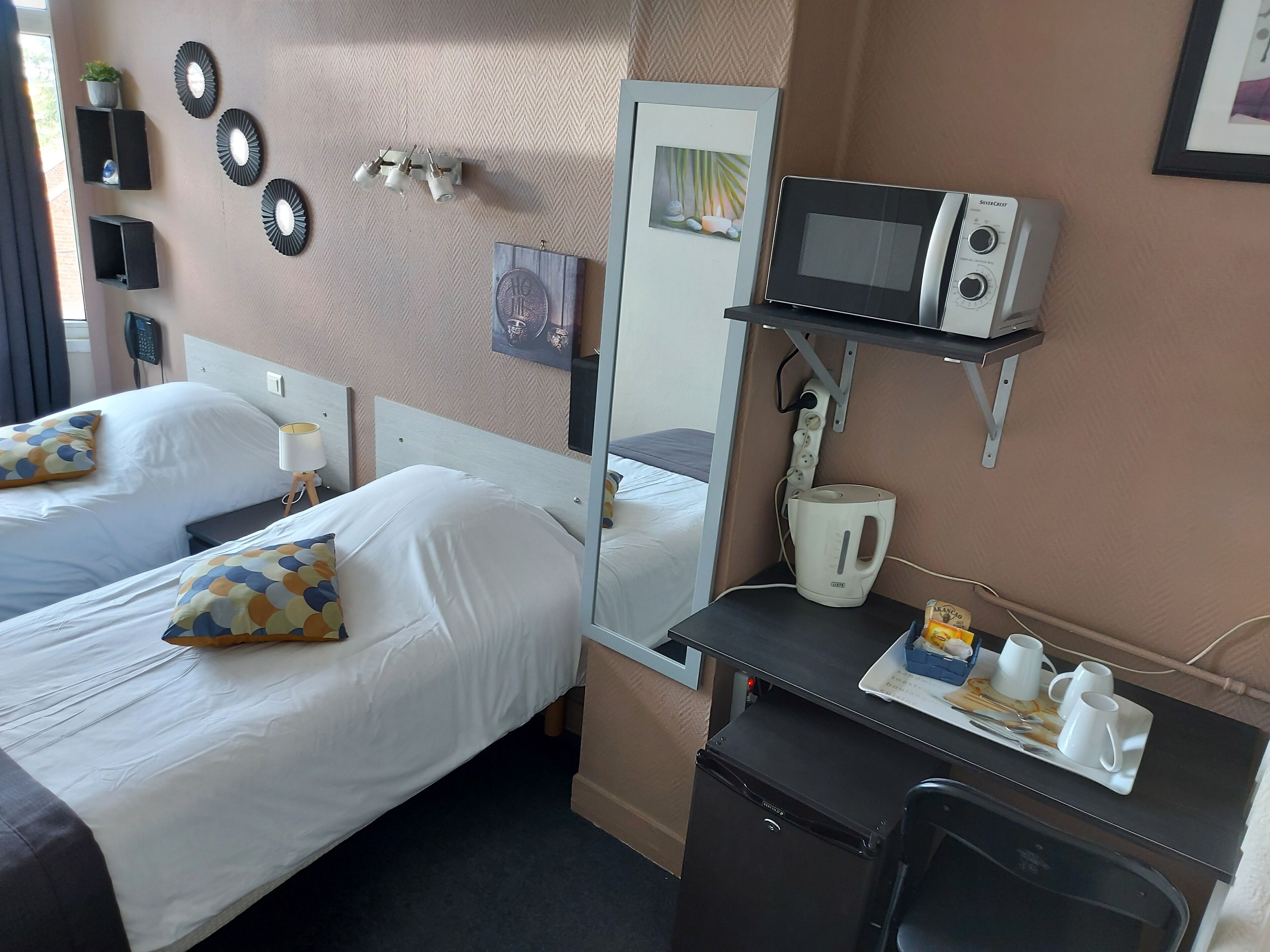 Een hotelkamer met twee bedden, een bureau met een magnetron, waterkoker en een kleine koelkast.