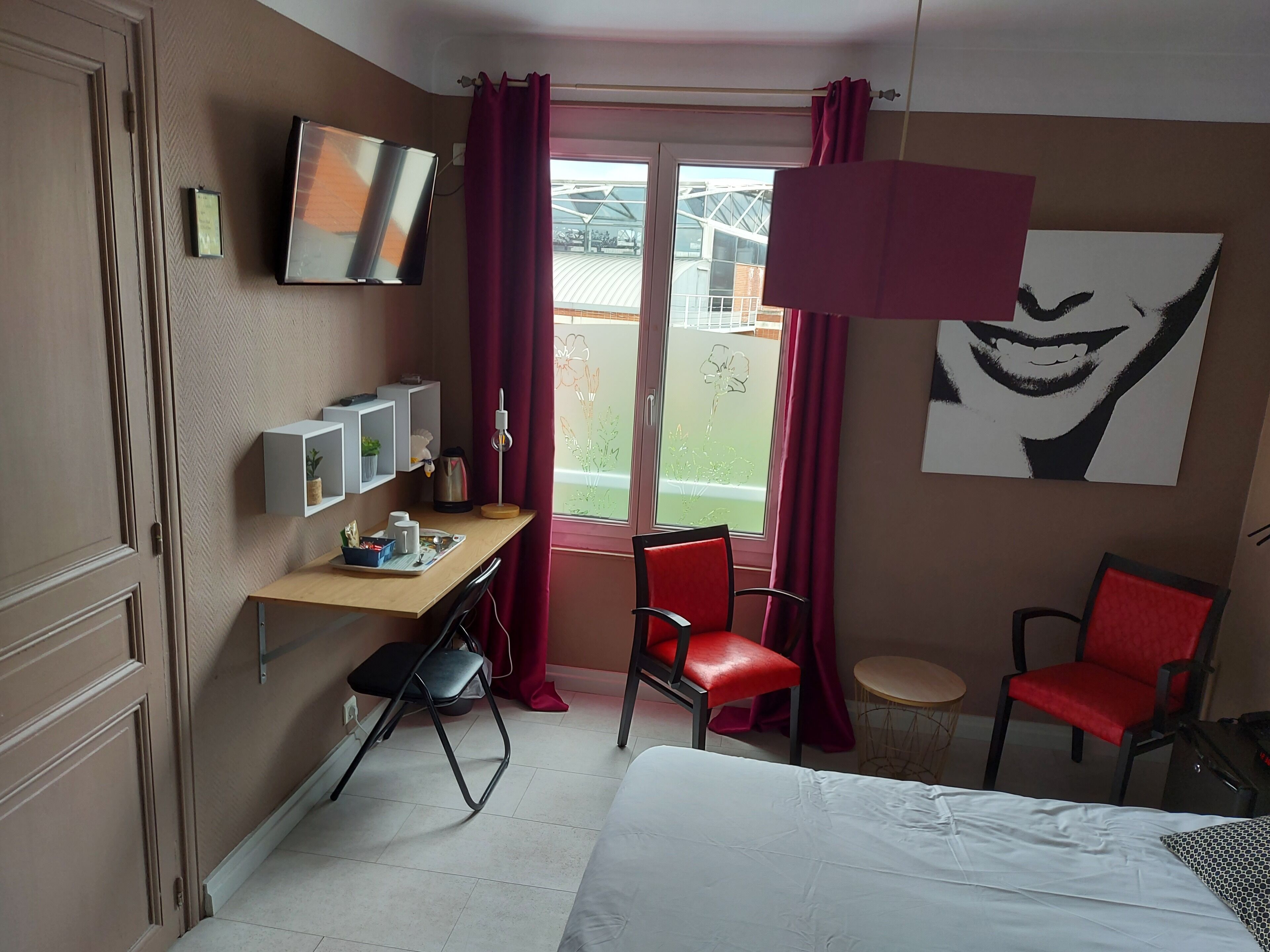 A hotel room with a bed, a desk with a chair, a TV, and a window with curtains.
