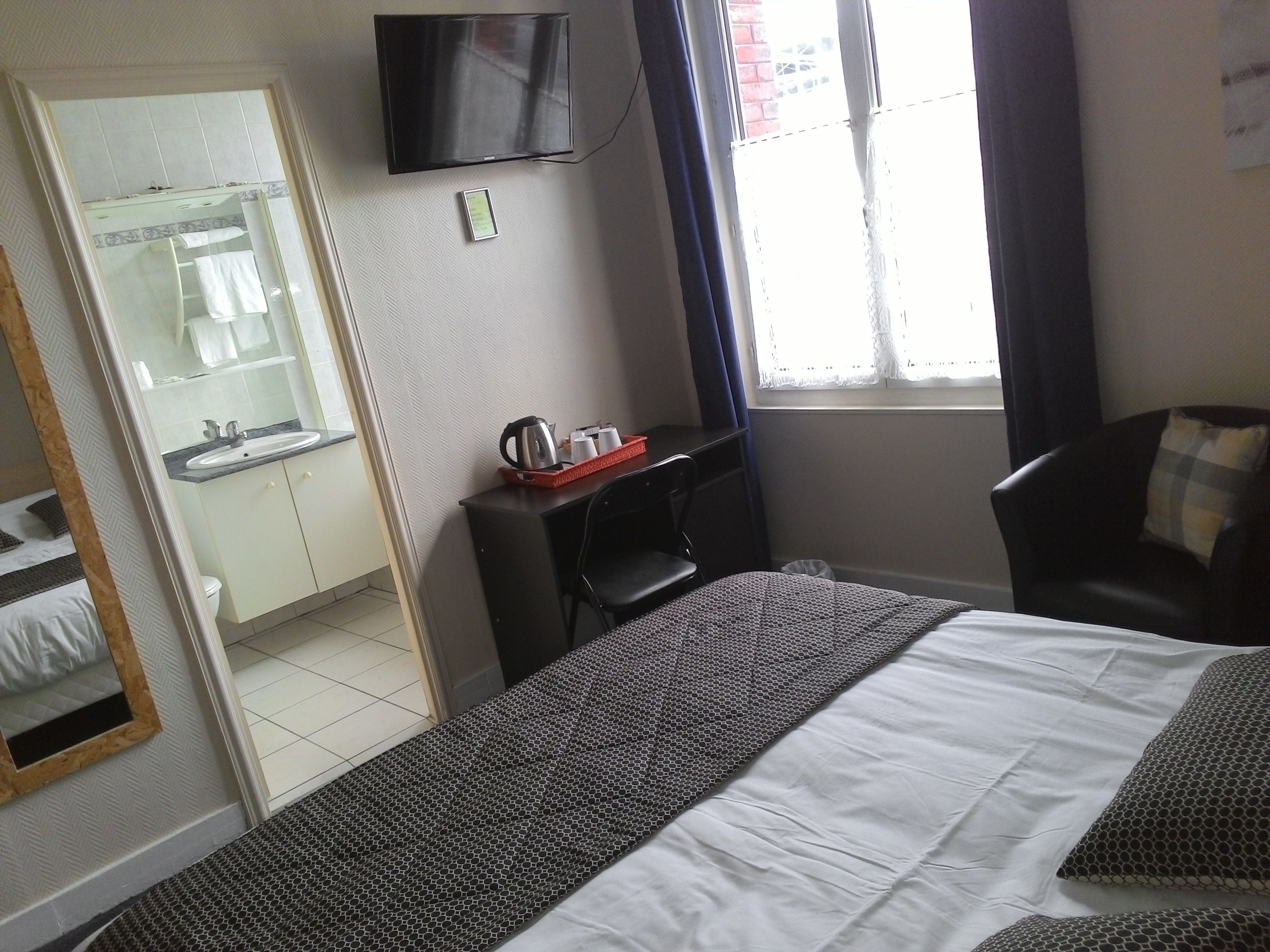 Hotelkamer met een bed, bureau, stoel, televisie, raam en een badkamer zichtbaar door een geopende deur.