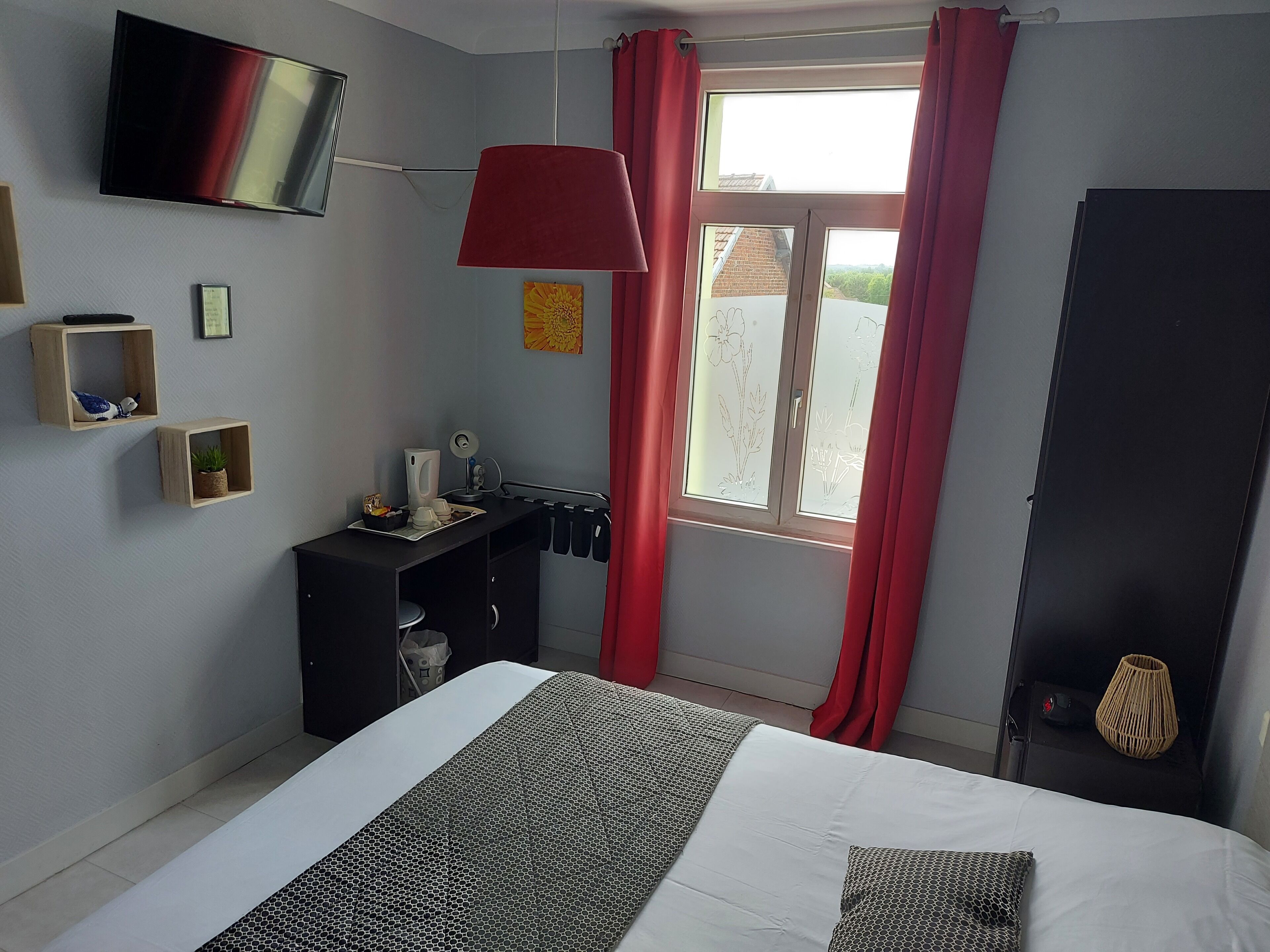 Een slaapkamer met een bed, een bureau, een televisie en een raam met gordijnen.