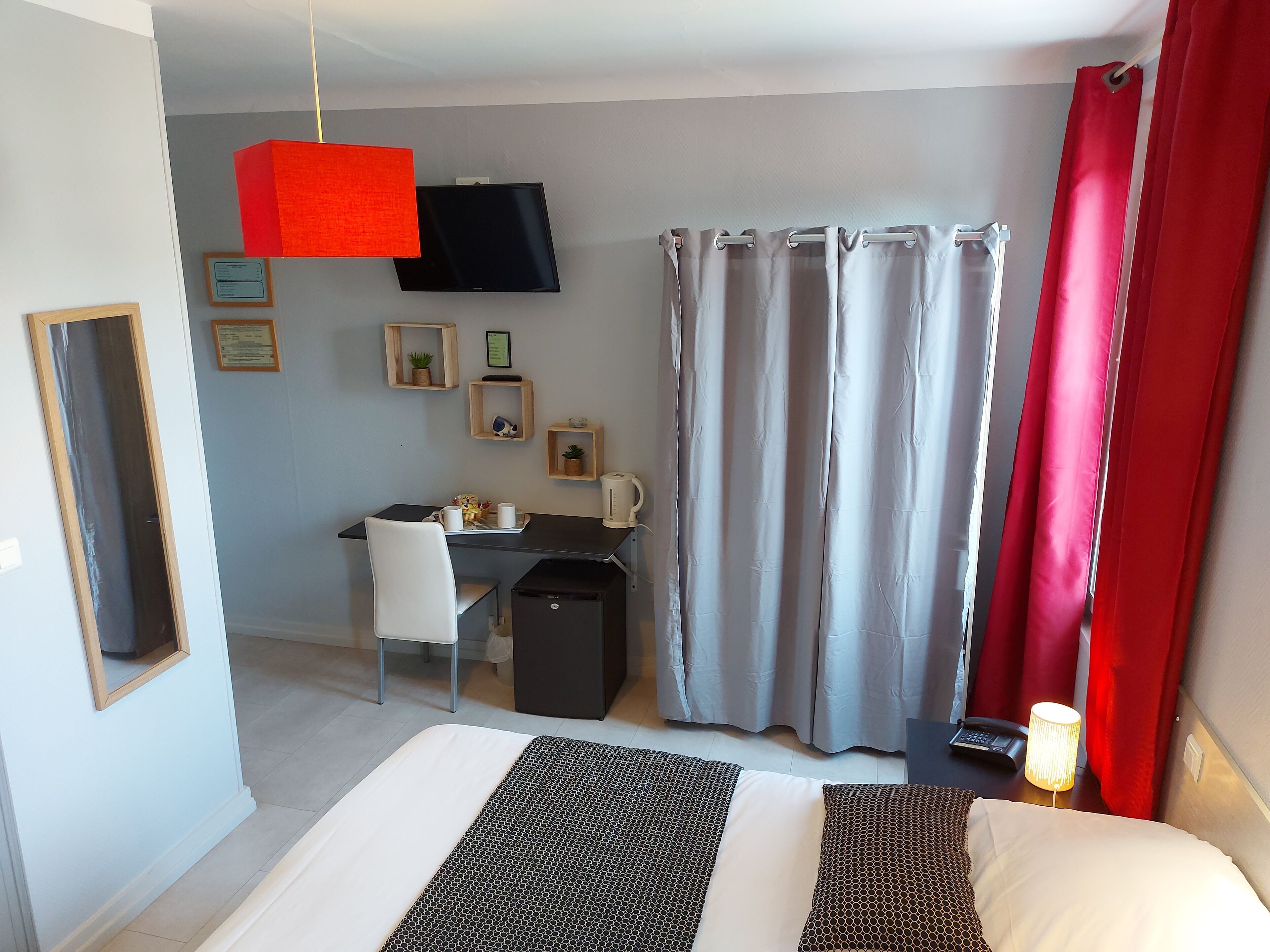 A hotel room with a bed, a desk with a chair, a television, and a window with curtains.