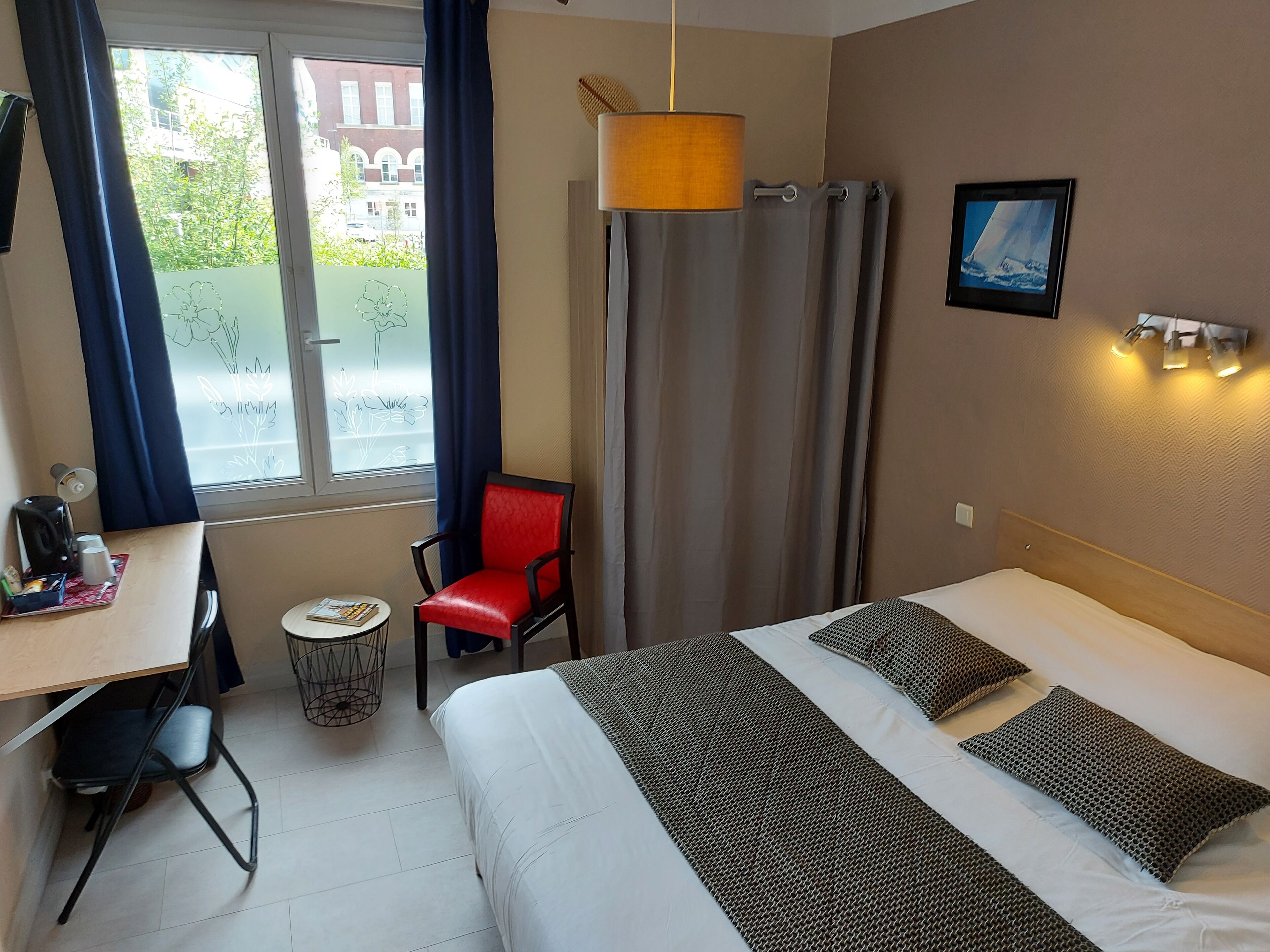 Ein Hotelzimmer mit Bett, Schreibtisch, Stuhl, kleinem Tisch und einem Fenster mit Vorhängen.