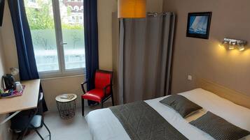 Ein Hotelzimmer mit Bett, Schreibtisch, Stuhl, kleinem Tisch und einem Fenster mit Vorhängen.