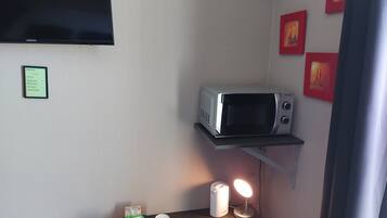 A small kitchenette with a microwave on a shelf, a table with cups and a tea bag, and a wall-mounted TV.