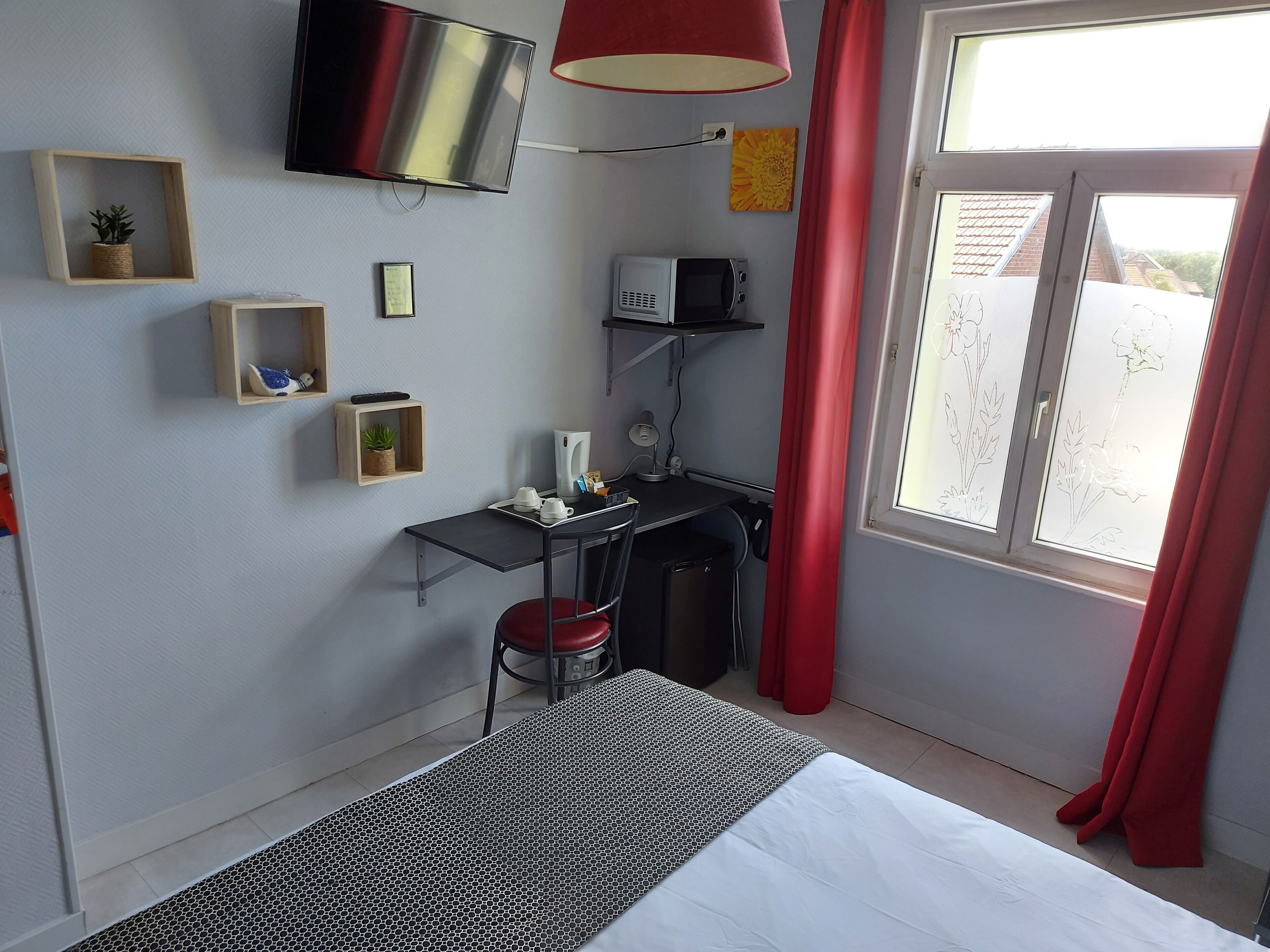 Ein Hotelzimmer mit Bett, Schreibtisch mit Stuhl, einem an der Wand montierten Fernseher und einem Fenster mit Vorhängen.