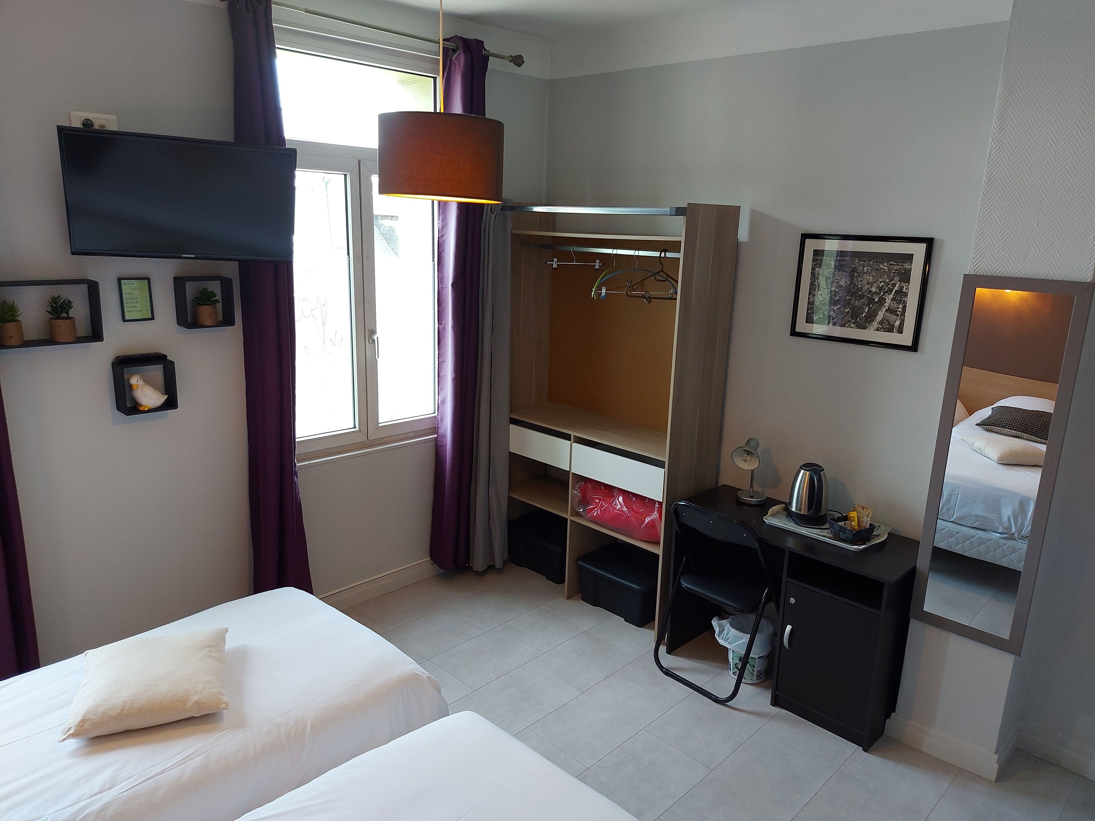 A hotel room with a bed, a desk with a chair, a wardrobe, a television, and a window with curtains.