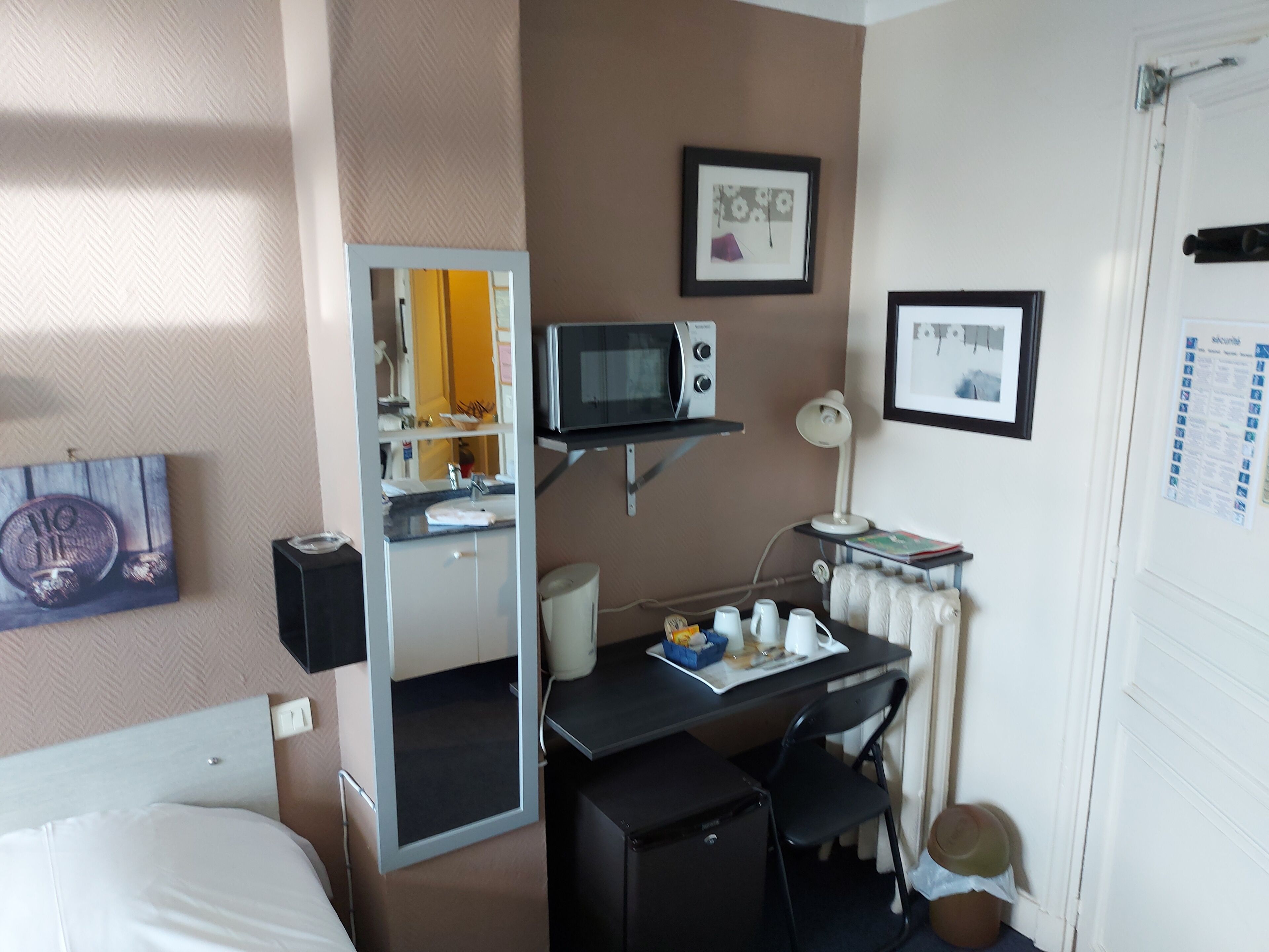 Une chambre d’hôtel de taille réduite, comprenant un lit, un bureau avec un ordinateur, un four à micro-ondes et une petite chaise.