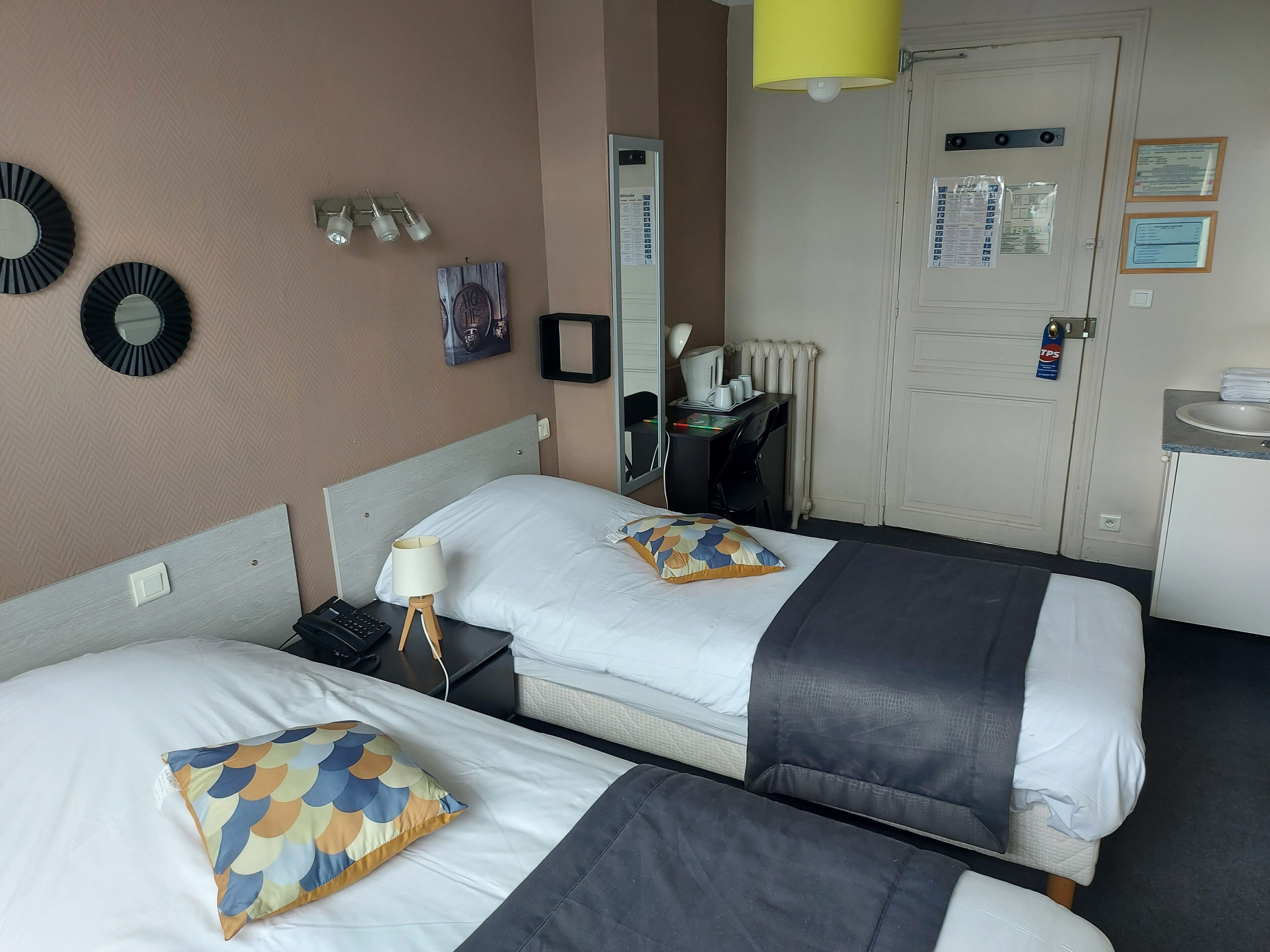 A hotel room with two beds, a desk, a chair, a lamp, and a mirror.