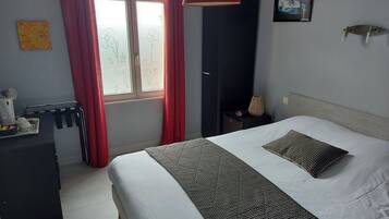 Habitación de hotel con cama, mesita de noche, escritorio, silla, ventana con cortinas y lámpara de pared.