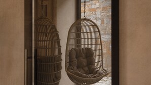Een kamer met een hangstoel, een hanglamp en uitzicht op buiten.