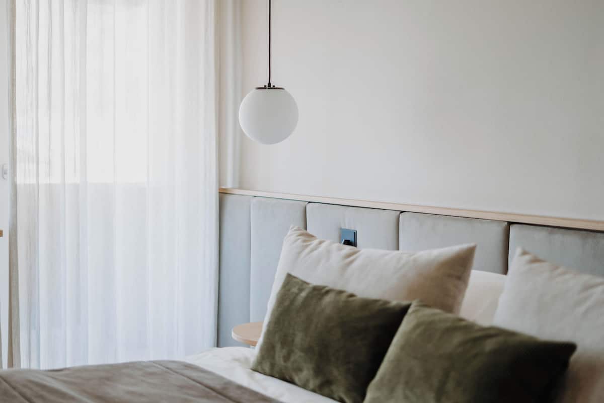 Een slaapkamer met een bed, kussens, een nachtkastje en een hanglamp.