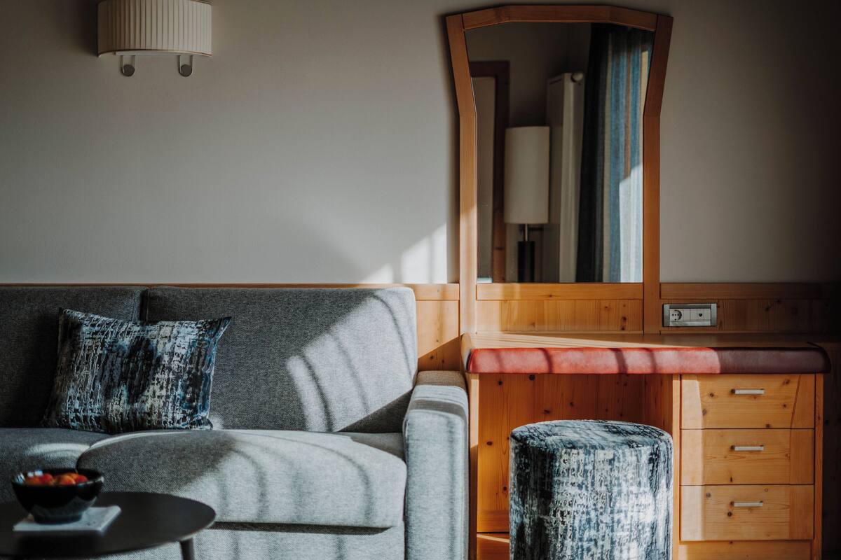 Een moderne woonkamer met een grijze bank, een houten bijzettafeltje, een spiegel en een klein krukje.
