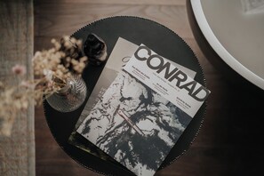 A magazine titled 'CONRAD' on a round black tray with a glass bottle and dried flowers beside it.