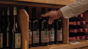 Ein Weinschränk aus Holz mit Flaschen, eine Hand, die nach einer Flasche greift, und Etiketten mit dem Wort 'PRESTIGE'.