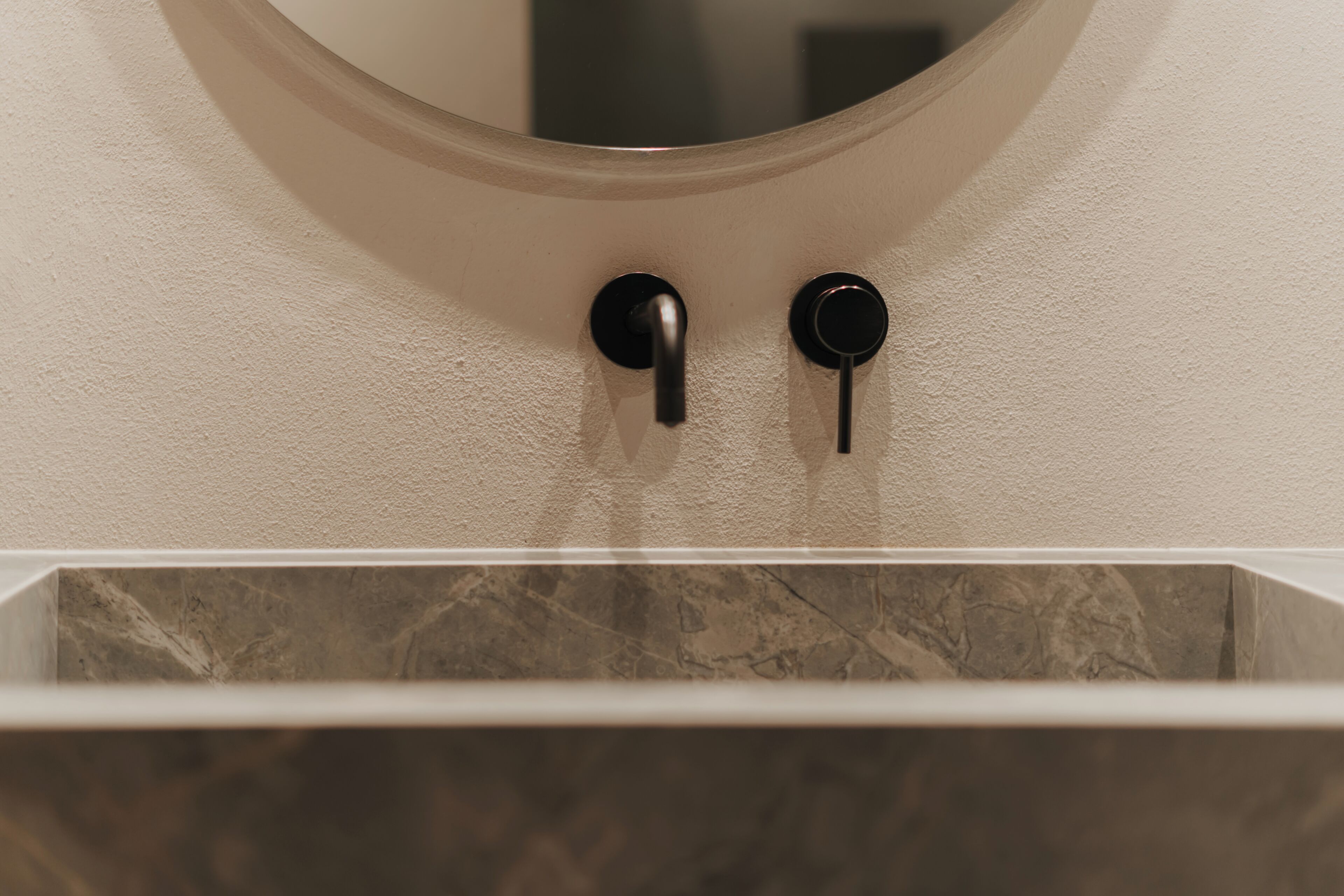 Une salle de bain avec un lavabo en marbre, un miroir rond et deux poignées noires.