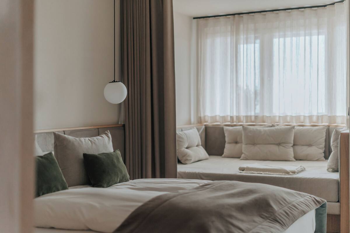 Een hotelkamer met een bed, nachtkastje, raam met gordijnen en een wandlamp.