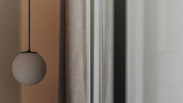 A modern room with a bed, a round pendant light, a small wooden table, and a curtain partially drawn.