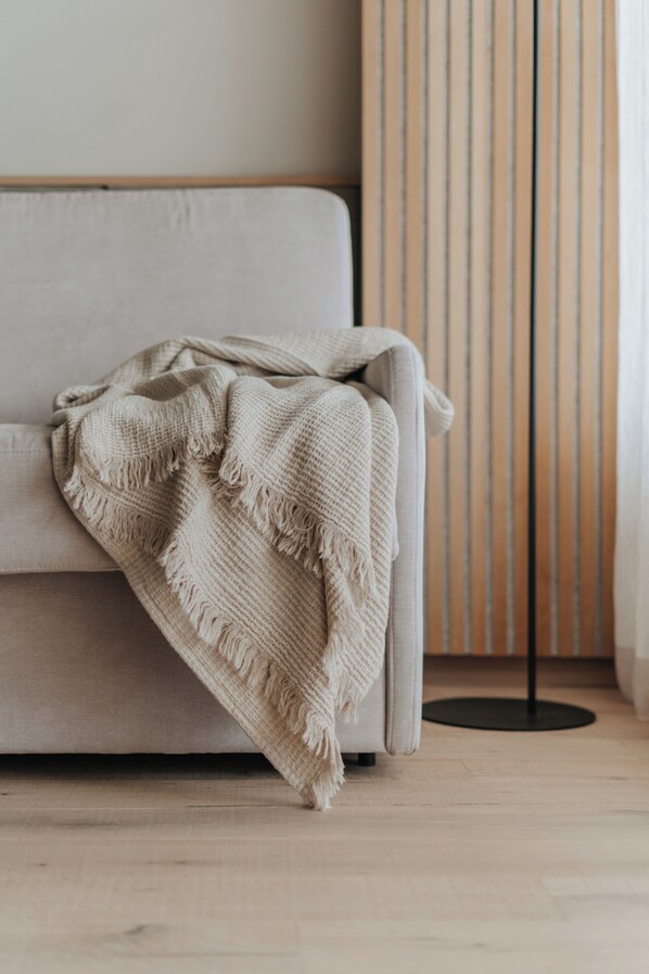 A sofa with a beige blanket, a floor lamp, and a wooden panel wall. - Das Paradies (Laces)