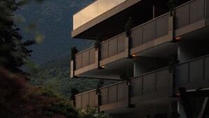 Een meerlaags gebouw met balkons, omgeven door groen en bergen op de achtergrond.