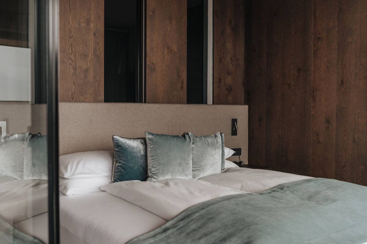 Een moderne slaapkamer met een houten hoofdbord, een bed met wit en grijs beddengoed, en een nachtkastje met een lamp.