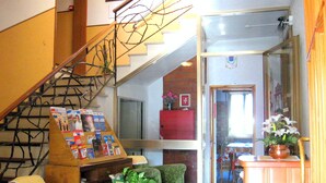 A lobby with a staircase, green armchairs, a wooden table with magazines, and a potted plant. - B&B Garnì Da Vito (Jesolo)