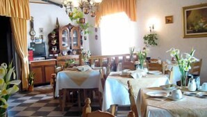 A dining area with checkered flooring, wooden tables, and chairs. There are potted plants and a clock on the wall. - B&B Garnì Da Vito (Jesolo)