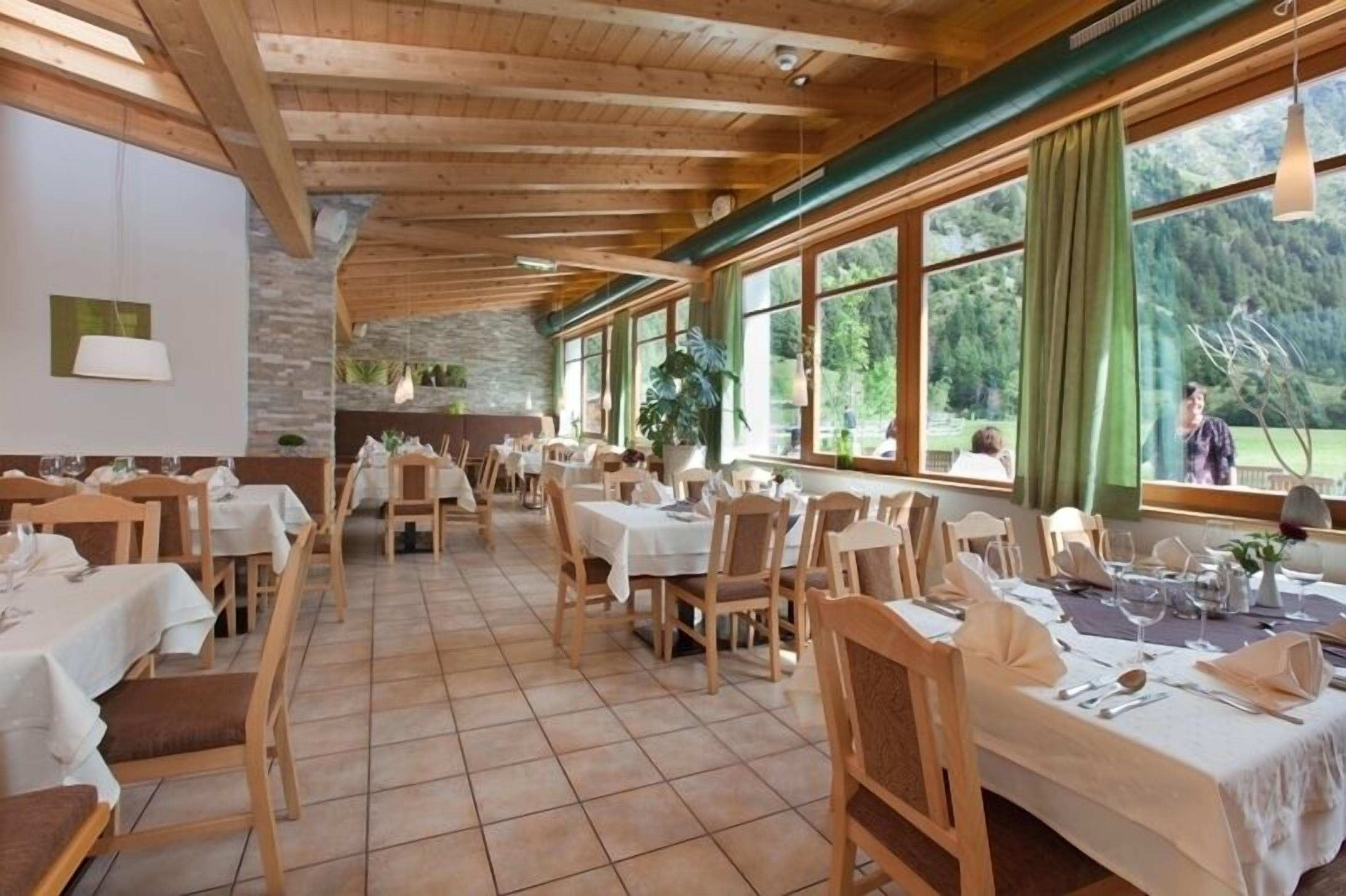 A restaurant with wooden beams, large windows, and a stone wall. Tables are set with white tablecloths and chairs.