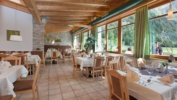 A restaurant with wooden beams, large windows, and a stone wall. Tables are set with white tablecloths and chairs.