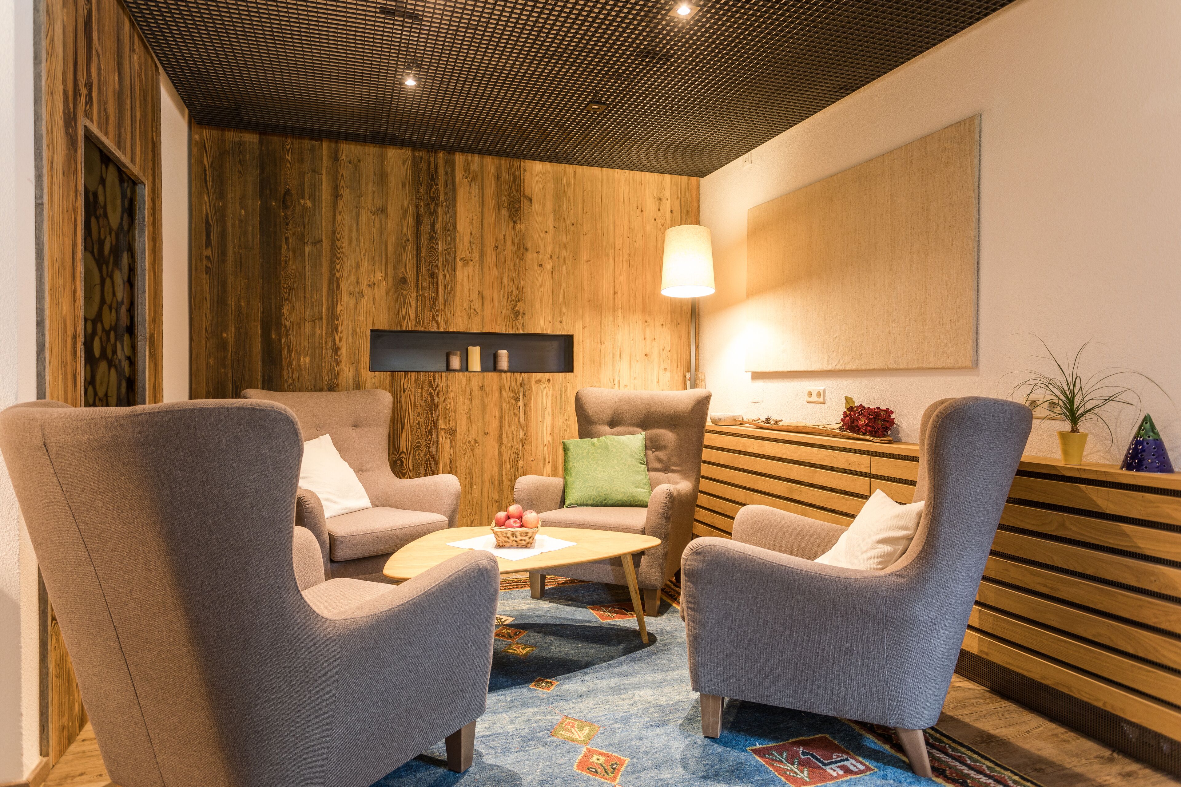 Una sala de estar moderna con una pared de acento de madera, una mesa redonda de centro y dos sillones grises.