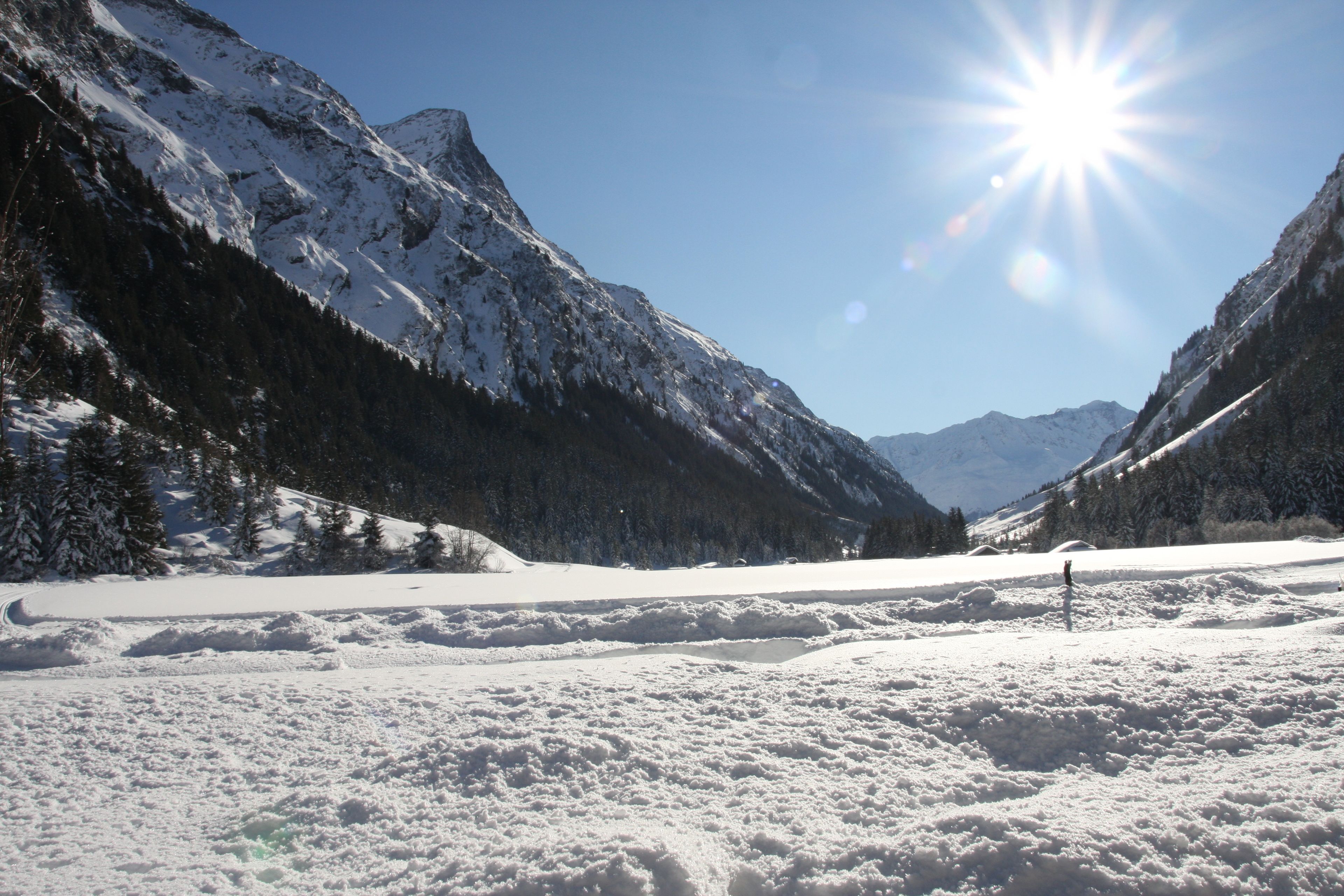 A snow-covered mountain landscape with a clear sky and a bright sun.