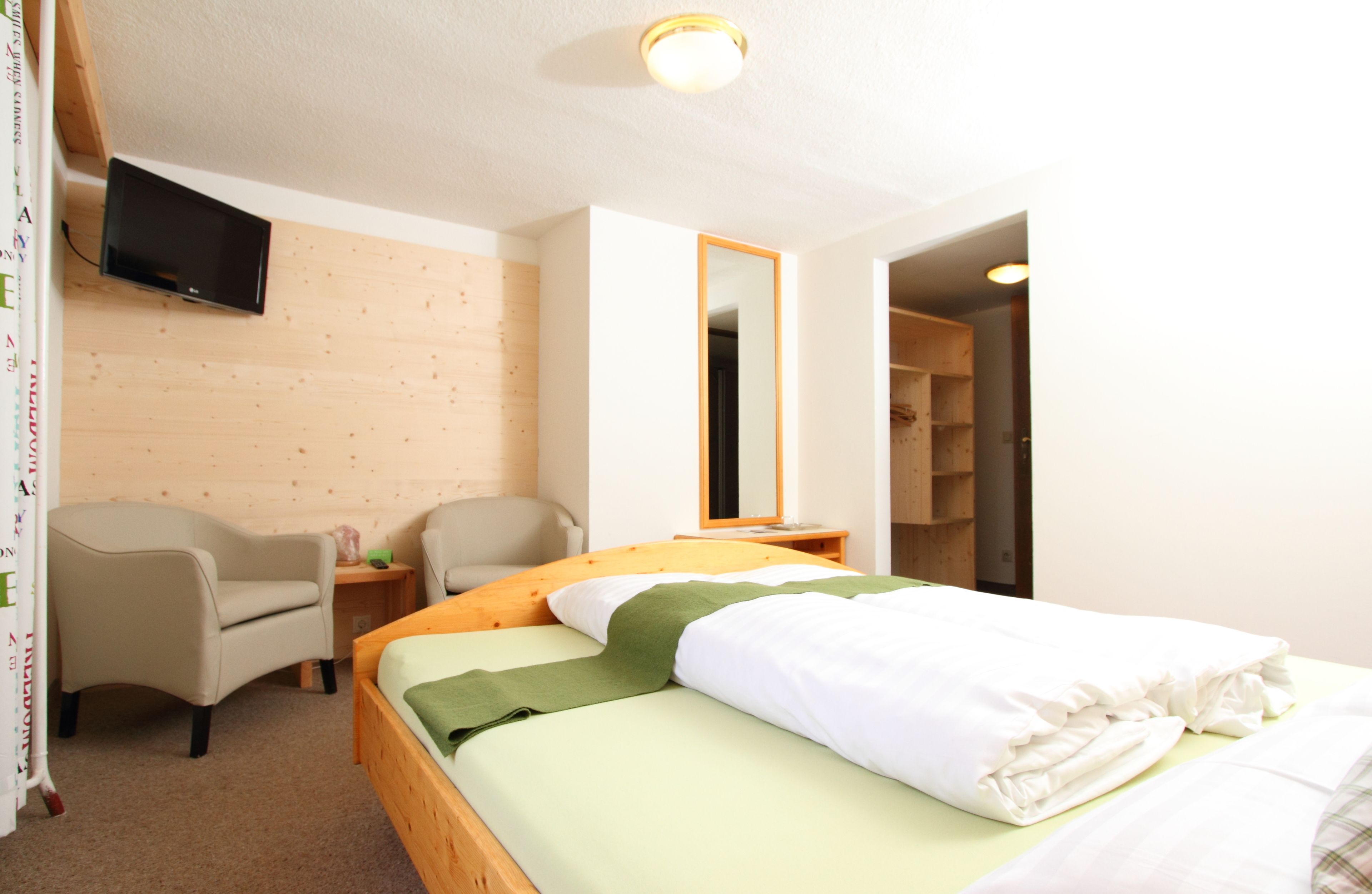 A hotel room with a bed, a chair, a TV mounted on the wall, and a mirror.